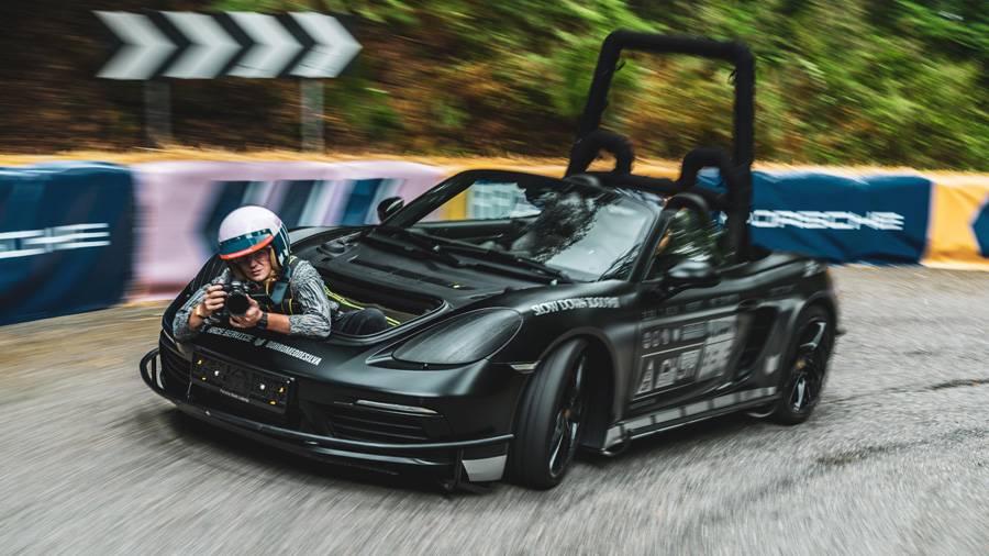 Au volant ? Personne. Le cadreur s’allonge dans le Porsche, mi-dans le vent, mi-dans la folie – pendant que le Boxster se transforme en studio roulant sur la route de montagne.