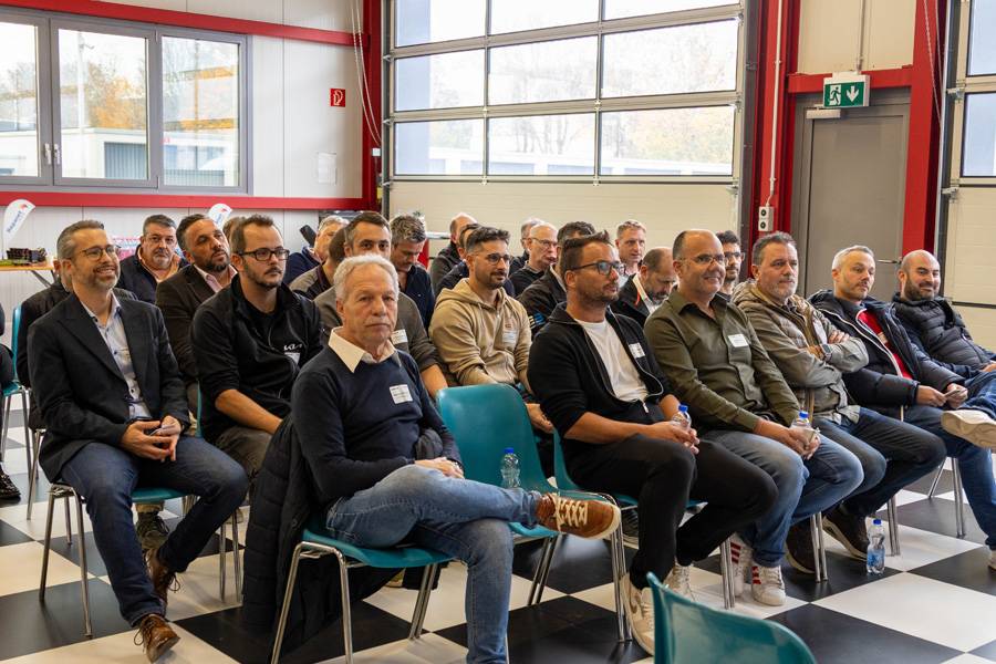 Volle Aufmerksamkeit zwischen Hebebühnen und Hochglanz: Die Helvetia-Netzwerkmitglieder lauschen konzentriert, als ginge es um den letzten Schliff am perfekten Lack. Fachwissen trifft Werkstattluft – genau die Mischung, die hier glänzt.