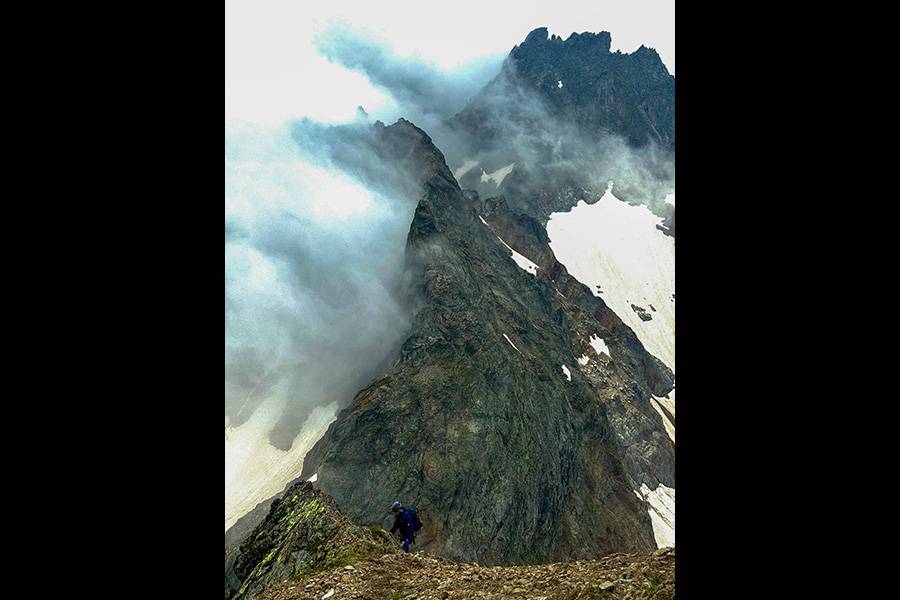Über dem Grat, wo Nebel und Fels ein stilles Duell ausfechten, arbeitet sich ein Alpinist Schritt für Schritt nach oben – ein Bild jener Entschlossenheit, die nur kennt, wer seine Wochenenden lieber hier als im Liegestuhl verbringt.