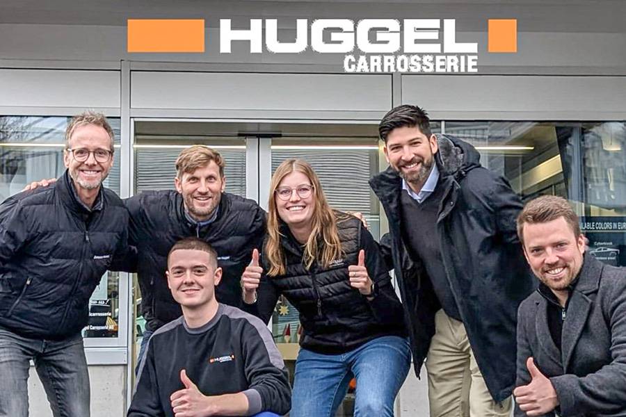 En route ensemble vers Shanghai : Davide Manieri et son coach Pascal Lehmann (tous deux agenouillés), entourés de l’équipe et des partenaires devant Huggel Carrosserie à Münchenstein — la Suisse envoie son espoir de la peinture aux WorldSkills.