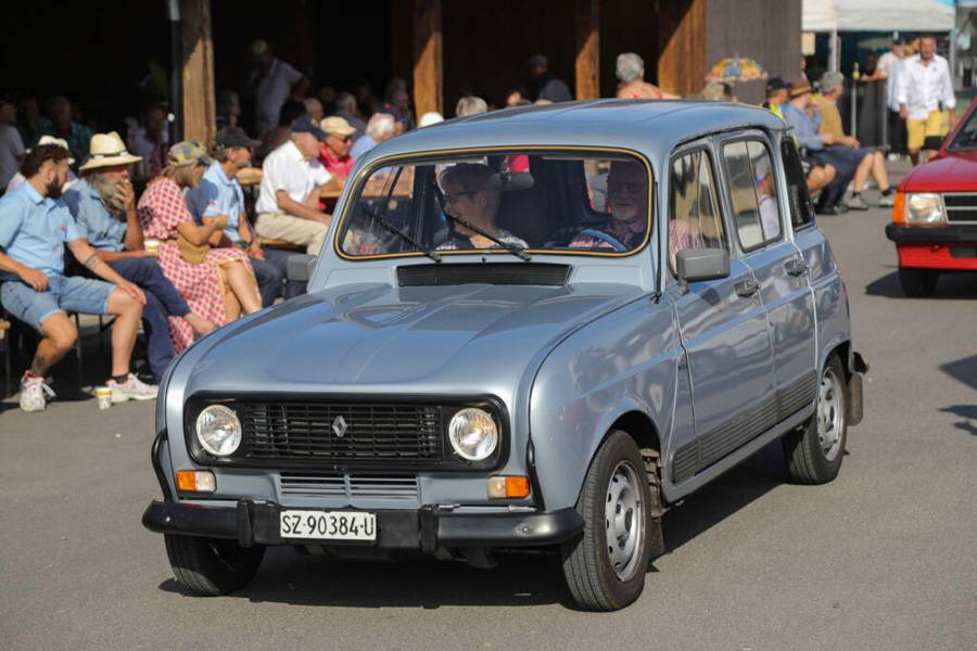 Une Renault 4 se faufile tranquillement dans une allée de bancs — l’histoire du quotidien à portée de main, entourée de spectateurs qui savent exactement pourquoi ils sont là.