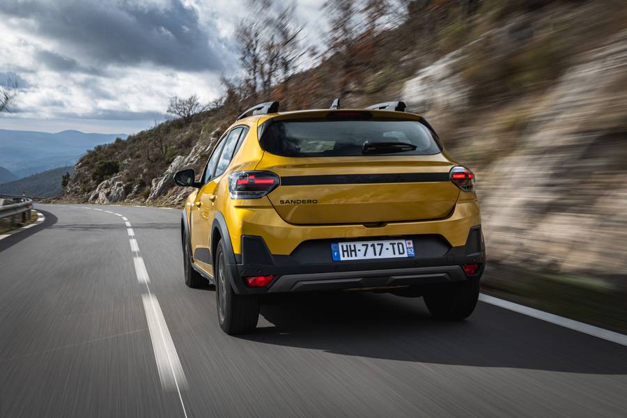 Vue arrière du Sandero Stepway en mouvement : entre les feux et le pare-chocs redessiné, une bande nervurée noir mat traverse toute la largeur du véhicule – un détail discret mais remarqué.