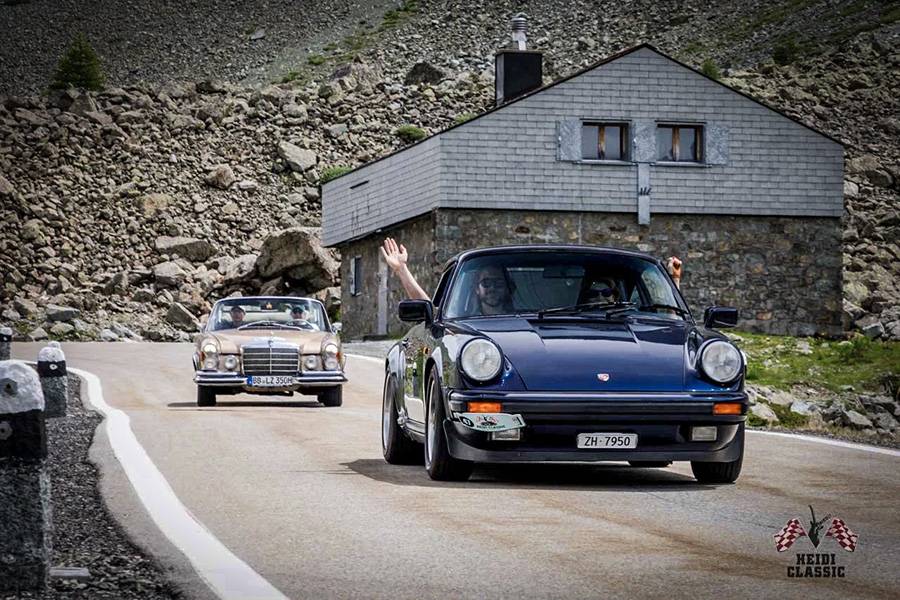Ein Porsche 911 auf Höhenkurs, dahinter ein klassischer Mercedes – so sieht Heidi Classic aus: Fahrfreude vor Felskulisse, Gelassenheit trotz Gipfelnähe und immer ein Hauch Abenteuer im Rückspiegel.