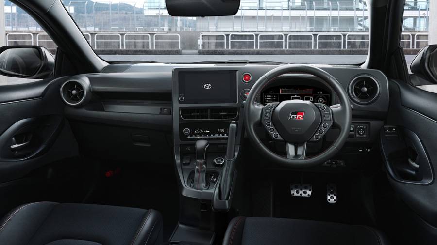 Dans le cockpit du GR Yaris, les commandes se rapprochent encore du conducteur. Outre le nouveau volant, plus compact et redessiné, c’est surtout le frein à main vertical, placé juste à côté du volant, qui attire le regard — un détail aux accents très clairement inspirés de la compétition.