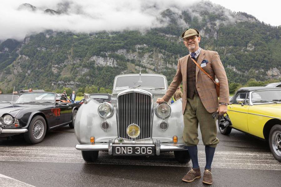 Sur fond alpin, un classique britannique aux lignes élégantes pose avec son propriétaire vêtu comme il se doit – exactement ce mélange de style, de tradition et de légère excentricité qui rend le British Car Meeting si attachant.
