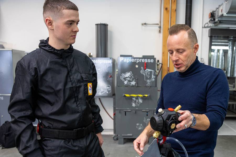Andreas Stocker zeigt Davide Manieri die Frischlufteinheit, die bereits mit dem Helm verbunden ist und ihn im Training mit sauberer Atemluft versorgt.