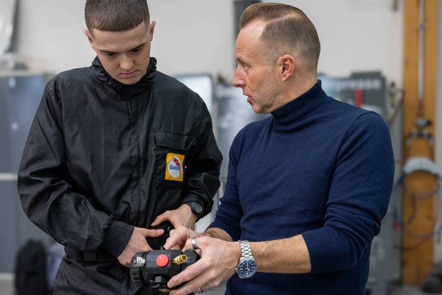 Andreas Stocker montre à Davide Manieri le compresseur, l’unité d’air frais du système : elle aspire l’air ambiant puis alimente le masque – et donc le peintre – en air frais respirable.
