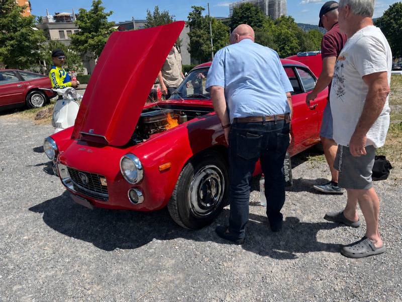 La romance dominicale vire soudain au sérieux: au moment où son propriétaire veut démarrer sa Lancia, des flammes surgissent du compartiment moteur. Heureusement, un amateur d’anciennes intervient aussitôt avec son extincteur.
