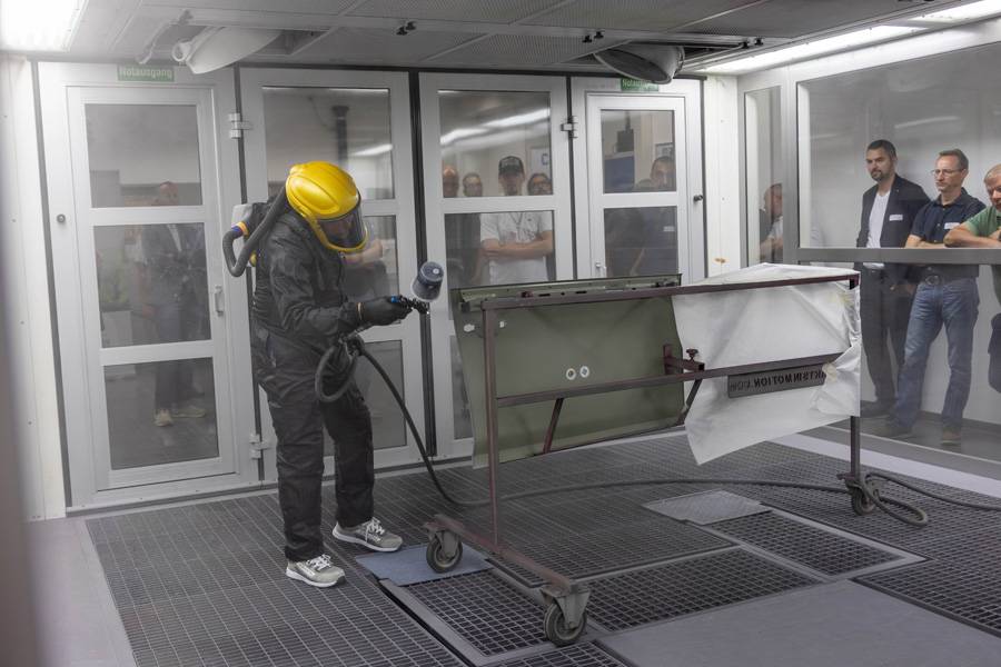Fabio Vicaro demonstriert mit gelbem Helm und Spritzpistole die Vorzüge vom «Autosurfacer Optima» von Sikkens an einem Carrosserieteil.