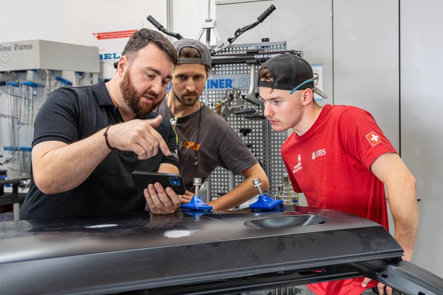 Antonino « Tony » Cipriano, André Schmid et Gilles Glauser s’entraînent avec le système de débosselage Car-O-Liner CDR-1. Sur leurs smartphones, ils suivent les différentes étapes de l’application et discutent ensemble de la marche à suivre.