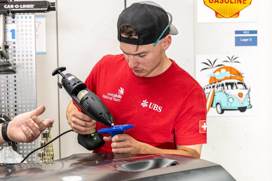 Gilles Glauser applique la colle sur l’adaptateur de traction bleu. Celui-ci est ensuite fixé sur la portière en aluminium de la BMW, afin de retirer la bosse de la tôle de manière contrôlée. 