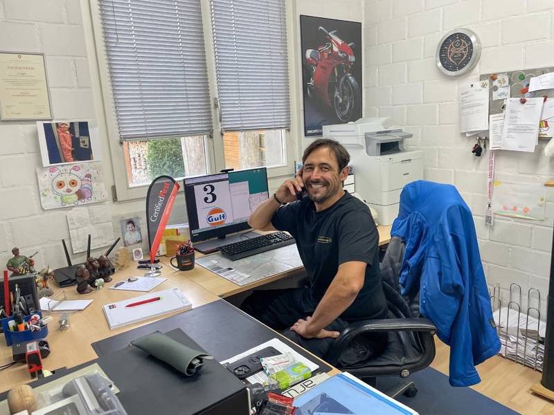 Alex Harder dans son bureau : tandis qu’à l’atelier, on ponce, mastique et peint, un travail bien fait commence souvent ici – au téléphone, devant l’écran, avec le prochain dossier de sinistre déjà posé sur la table. 
